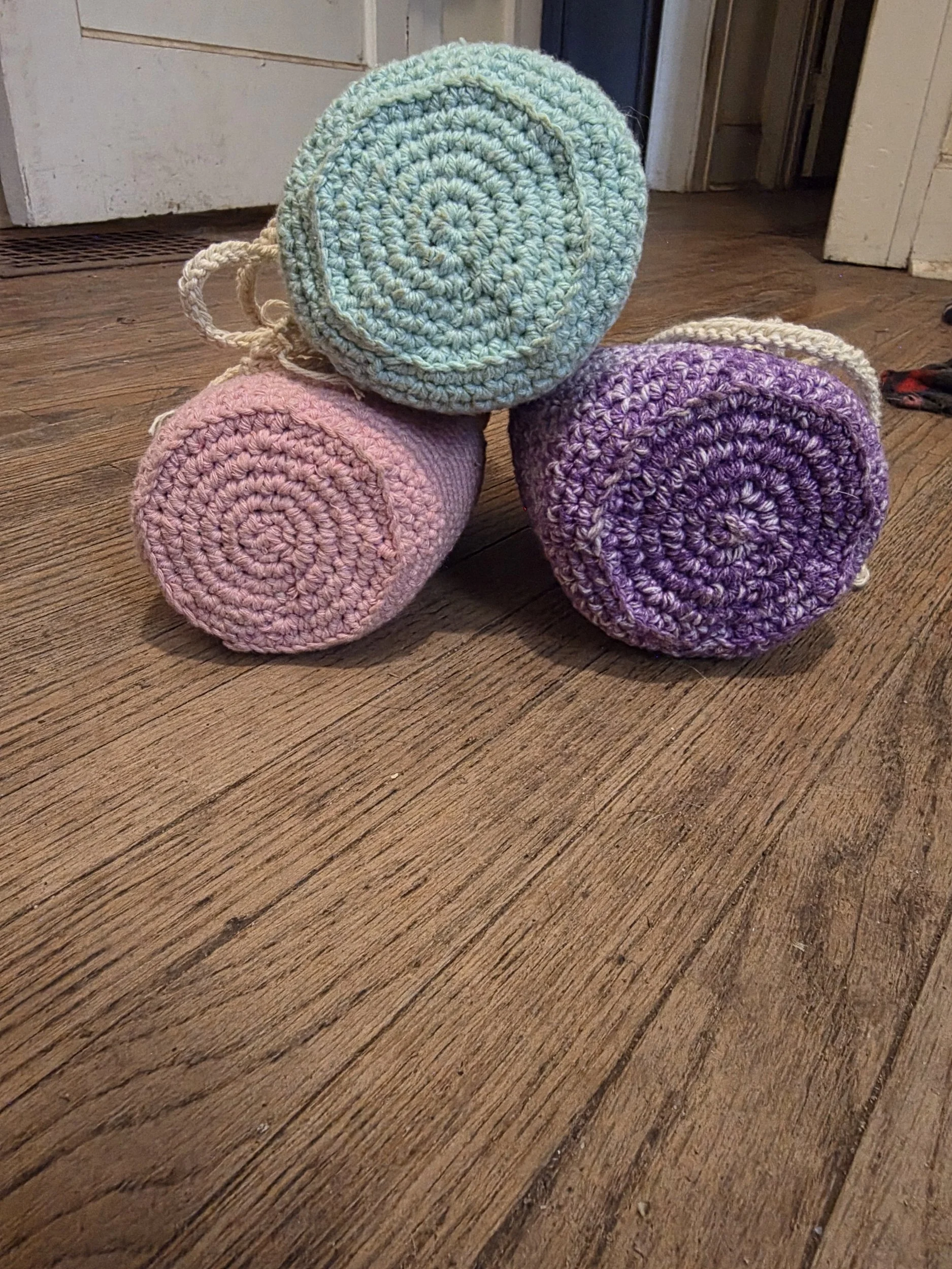 Bottom view of handmade crochet drawstring bags showing pink, blue, and purple bases