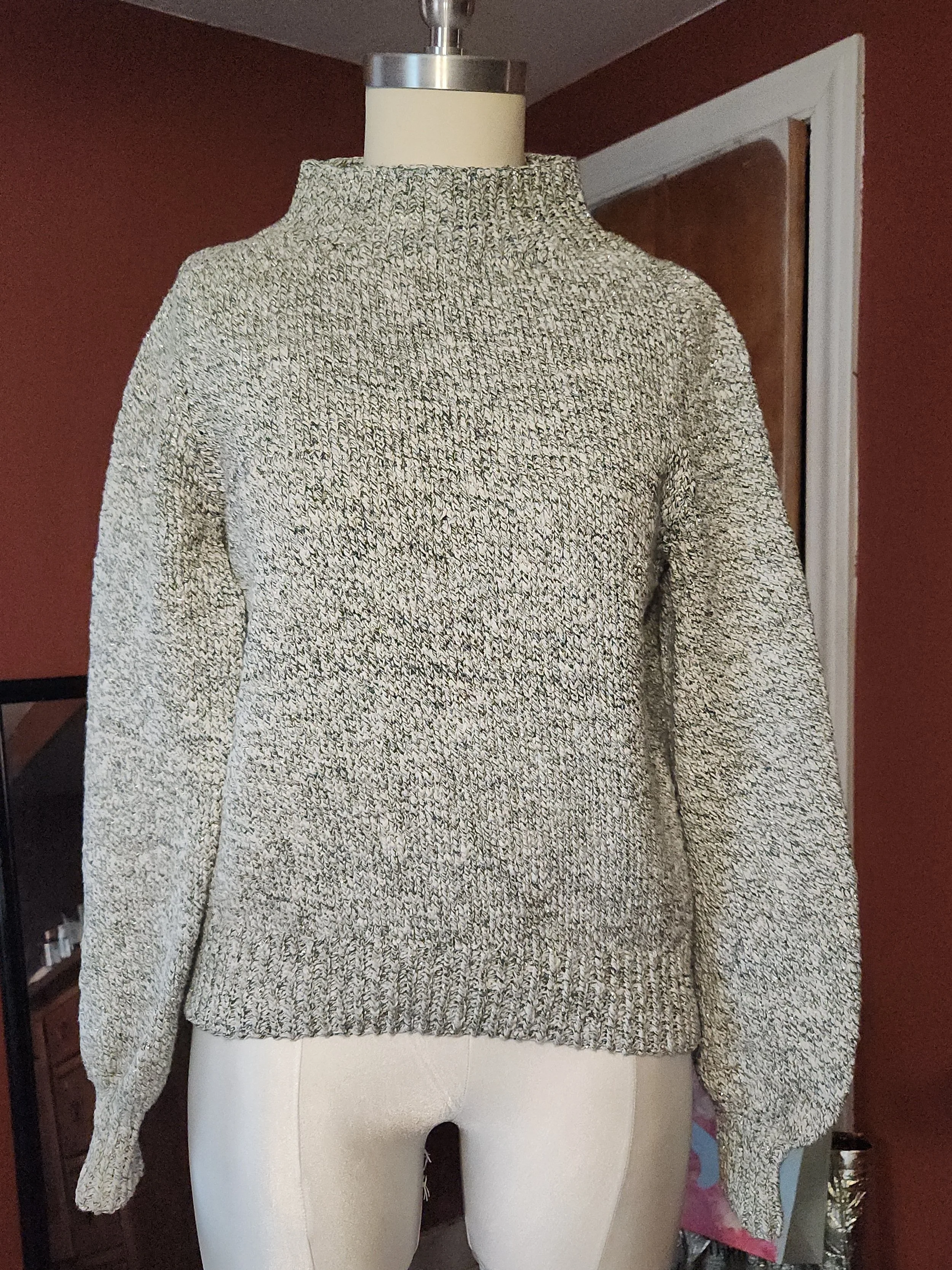 A mannequin wearing a speckled gray and cream knit sweater with a high collar and long sleeves.