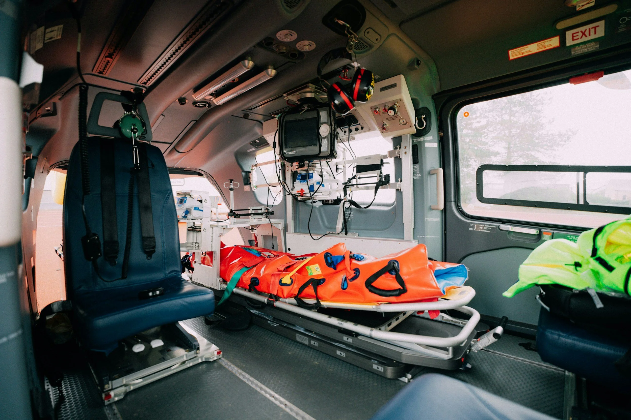 Interior of an ambulance with medical equipment, a stretcher with orange and blue padding, and seating for paramedics.