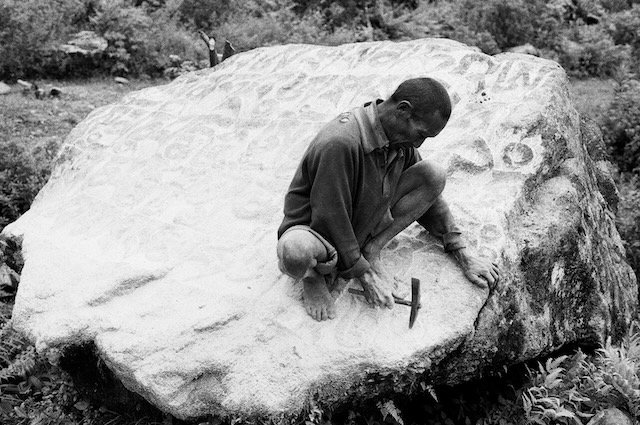 carving prayers into rock beside path