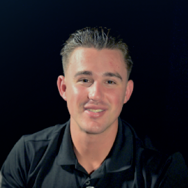 A young man with light skin, short slicked-back hair, wearing a black collared shirt, smiling at the camera against a dark background.