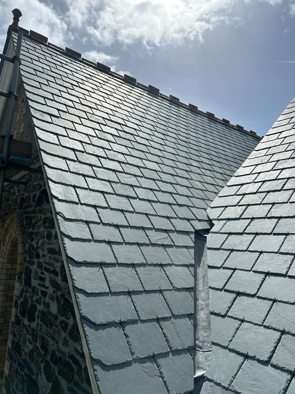Close-up of slate roofing on a building with a cloudy sky in the background.