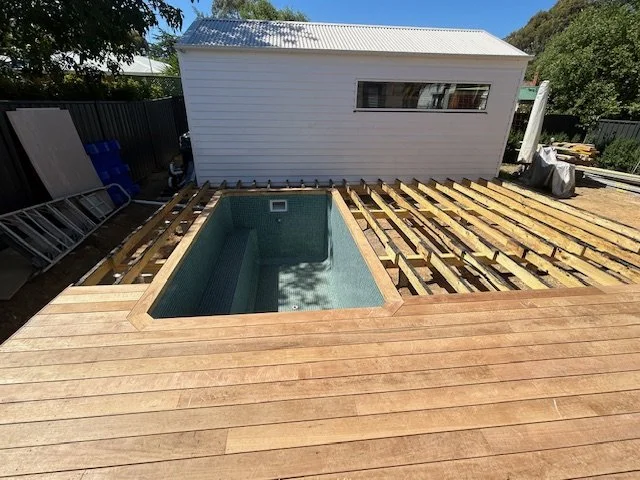 Decking partially under construction with a pool and a small building behind the deck.