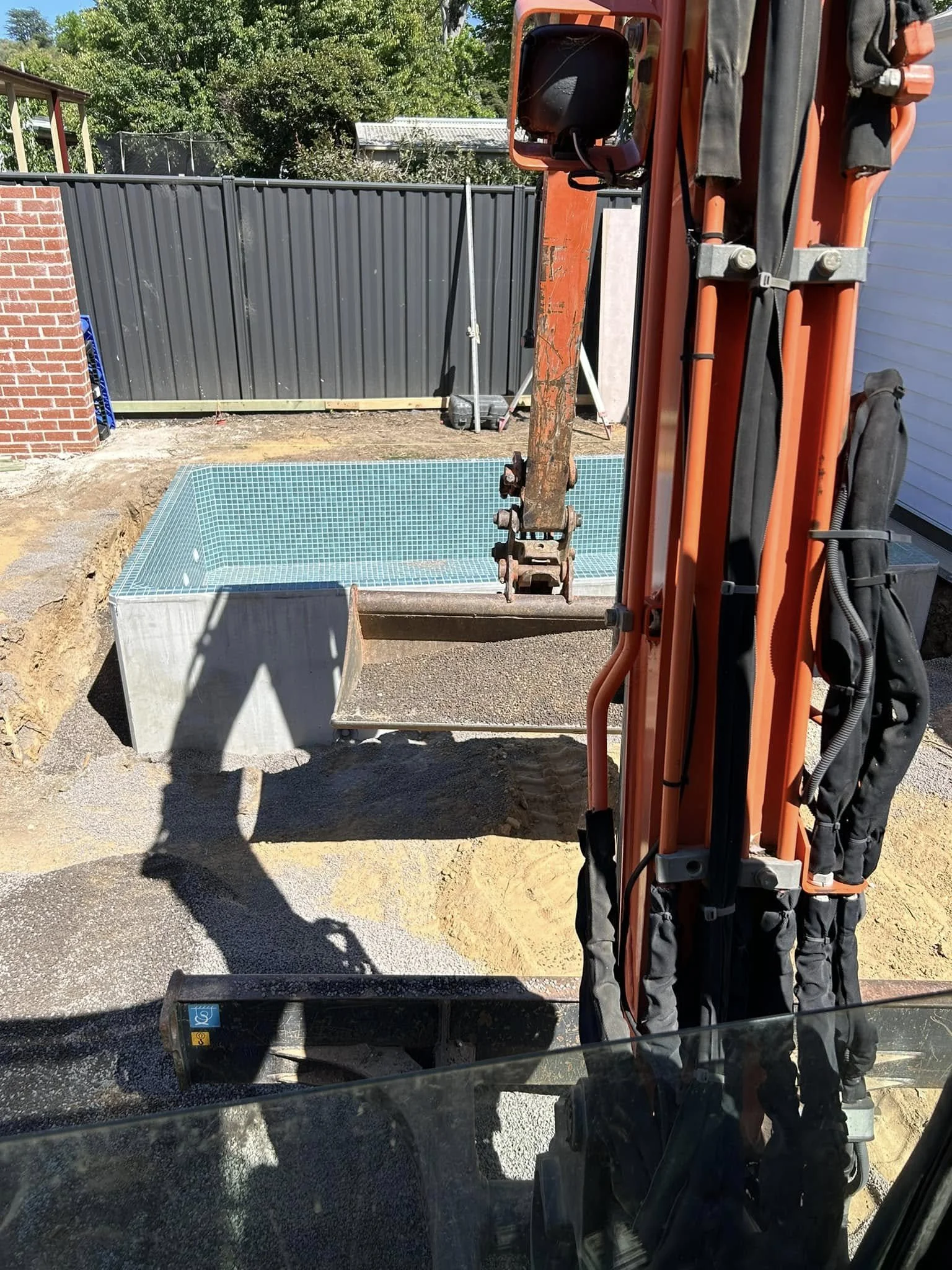 Construction site with excavator preparing to place a swimming pool with blue mosaic tiles into a backyard.