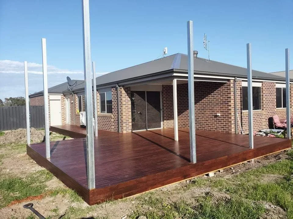 Wooden porch with pillars iin front a brick building.