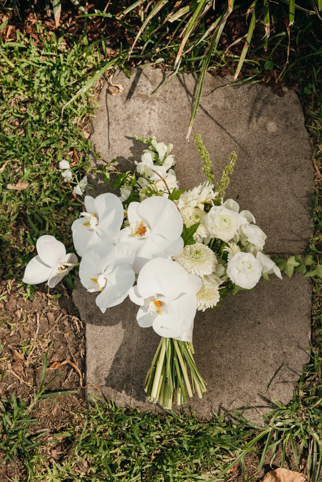 White floral bouquet with orchids and other flowers on a stone surrounded by grass.