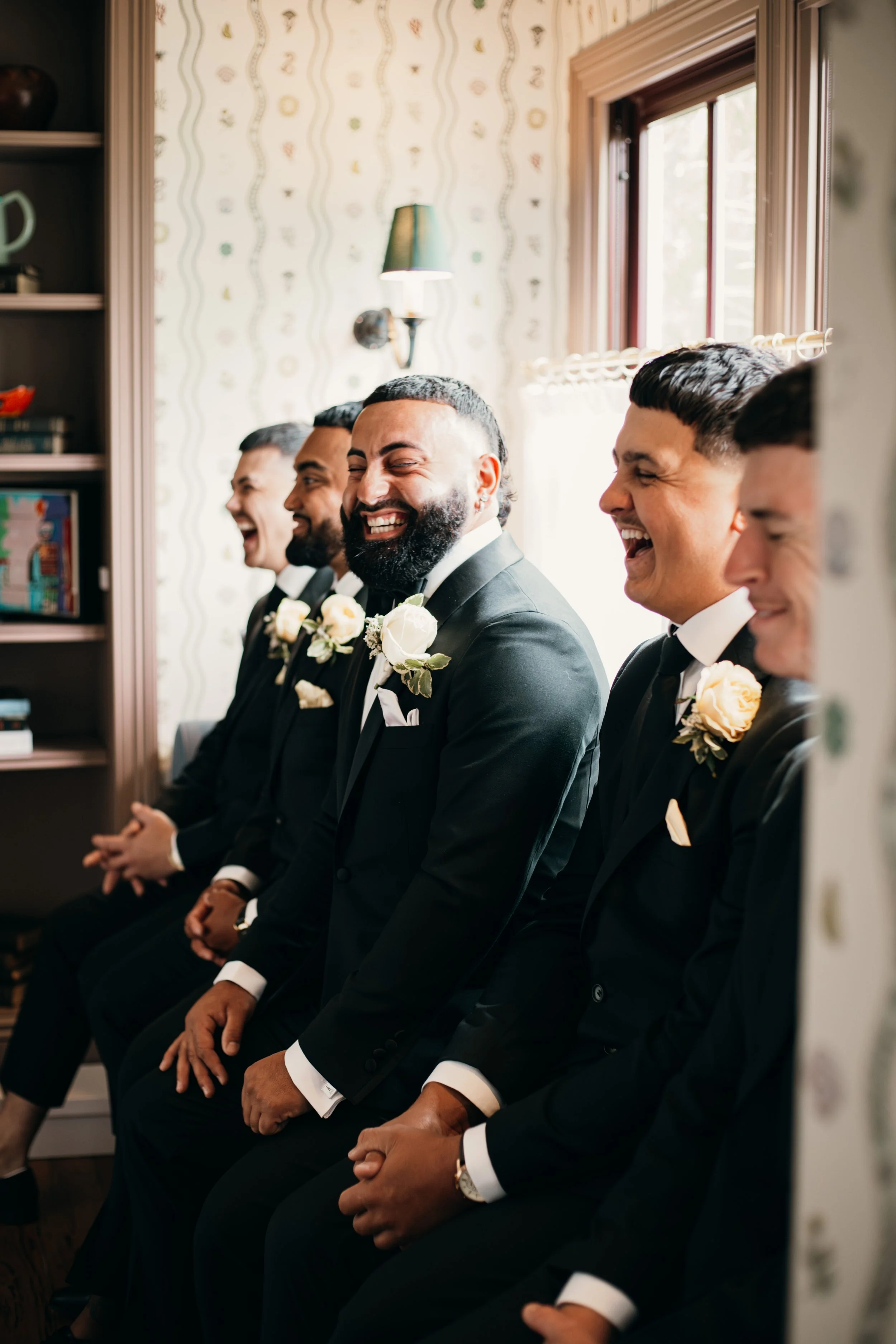 Group of men in black suits laughing and smiling during a wedding ceremony