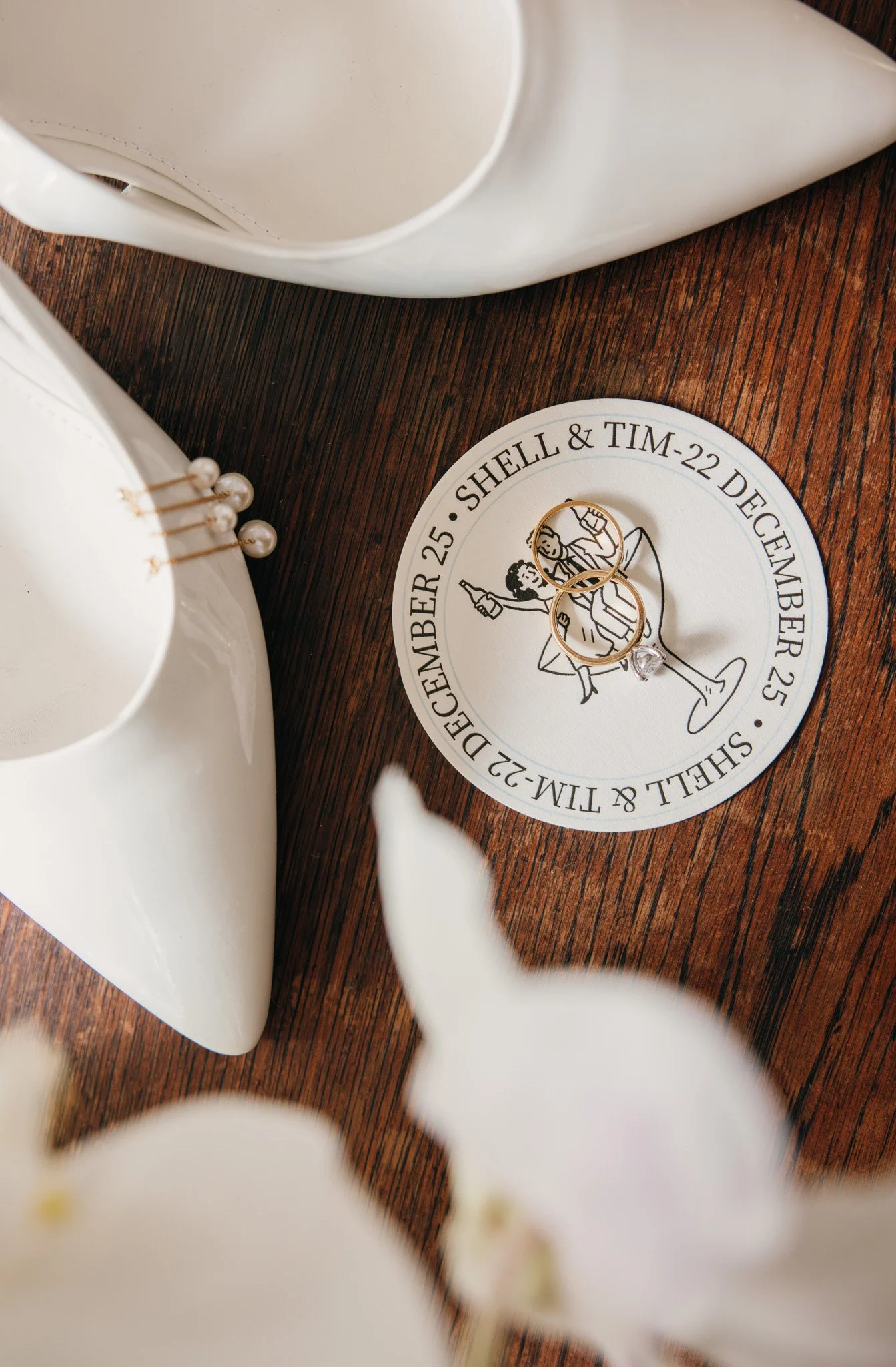 Wedding invitation with gold rings and white orchids on a wooden surface.