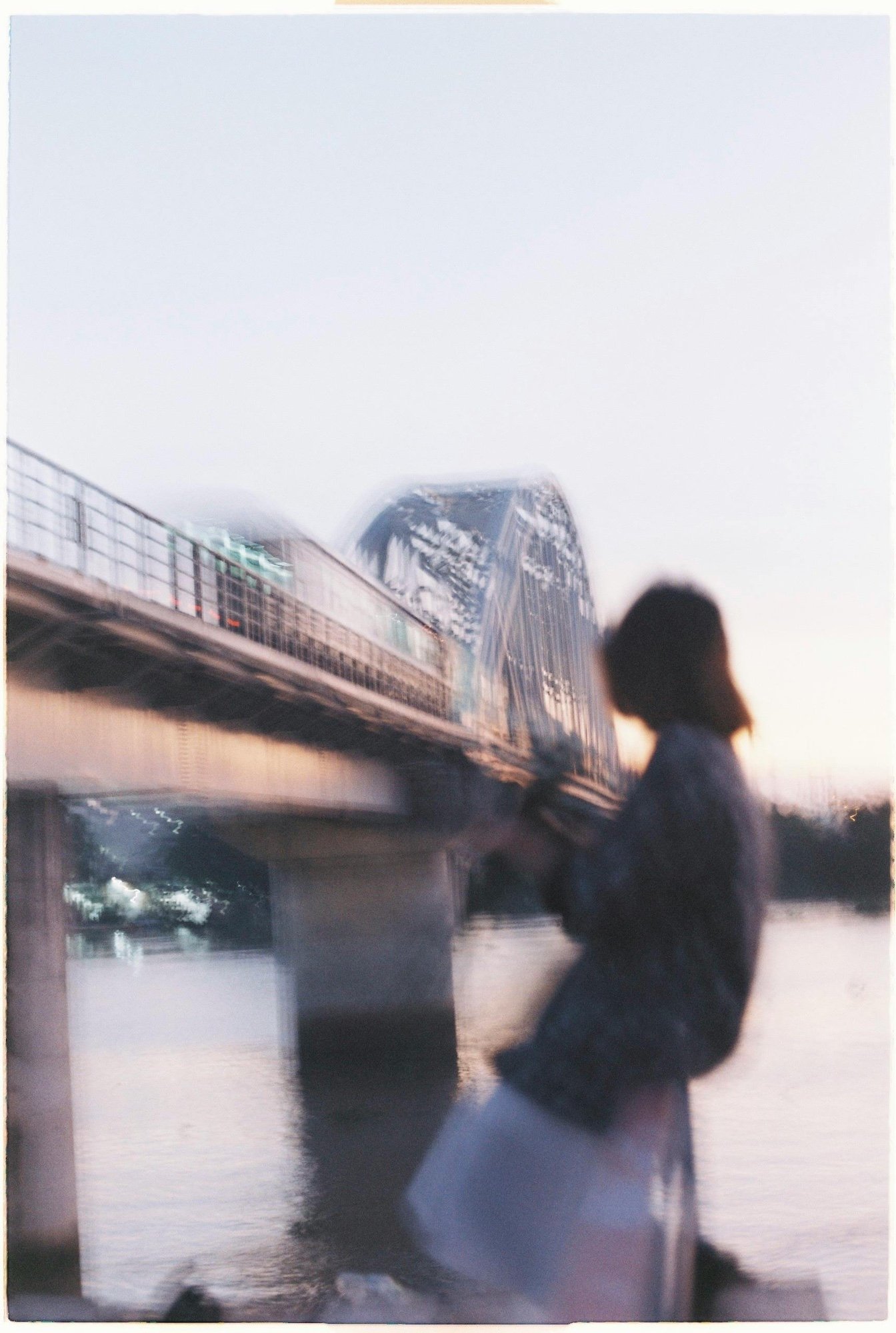 Photo d'une femme vue de dos qui regarde un pont dans une lumière de coucher de soleil violet