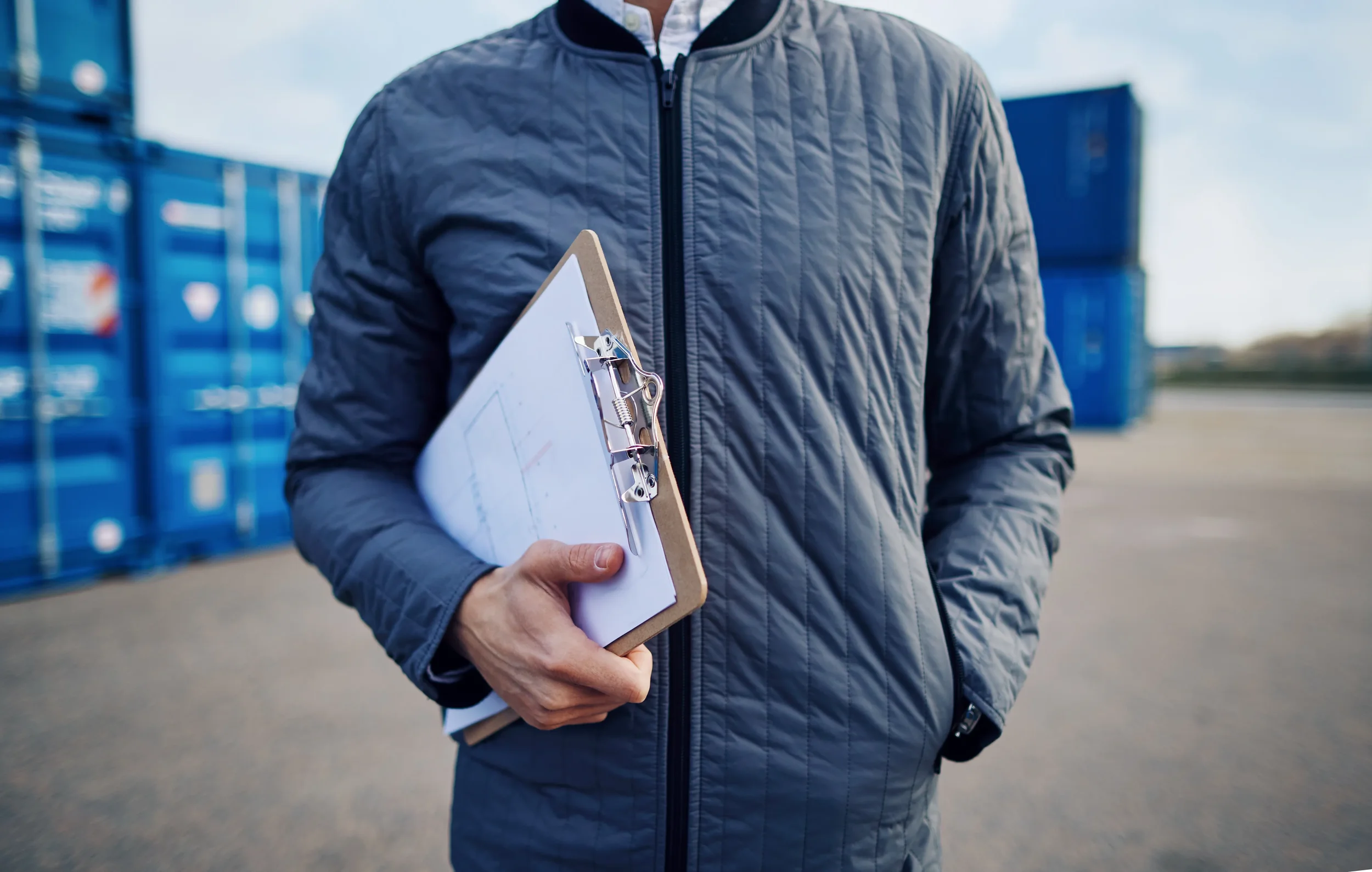 Close-up of a logistics operator's chest holding a clipboard with various inventory-related documents.