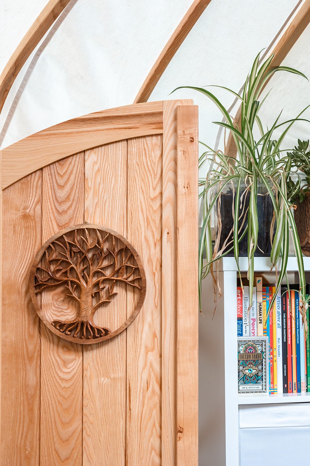 Wooden room divider with a carved tree design and a bookshelf with books and plants.