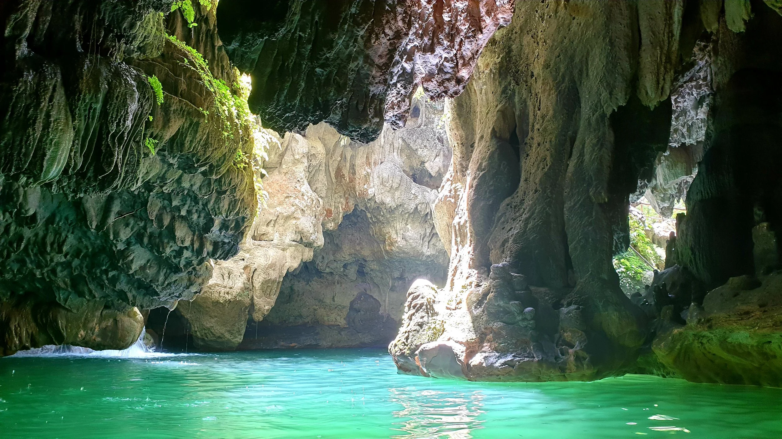 Intérieur d'une grotte dans l'eau à Trinidad avec des rochers et de l'eau turquoise, la lumière naturelle filtre à travers une ouverture, créant un contraste entre l'ombre et la lumière.