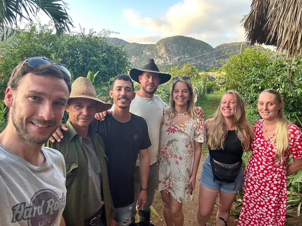 Groupe constitué de nos guides et clients, posant devant un paysage montagneux et verdoyant, avec un ciel partiellement nuageux, dans un environnement bucolique.