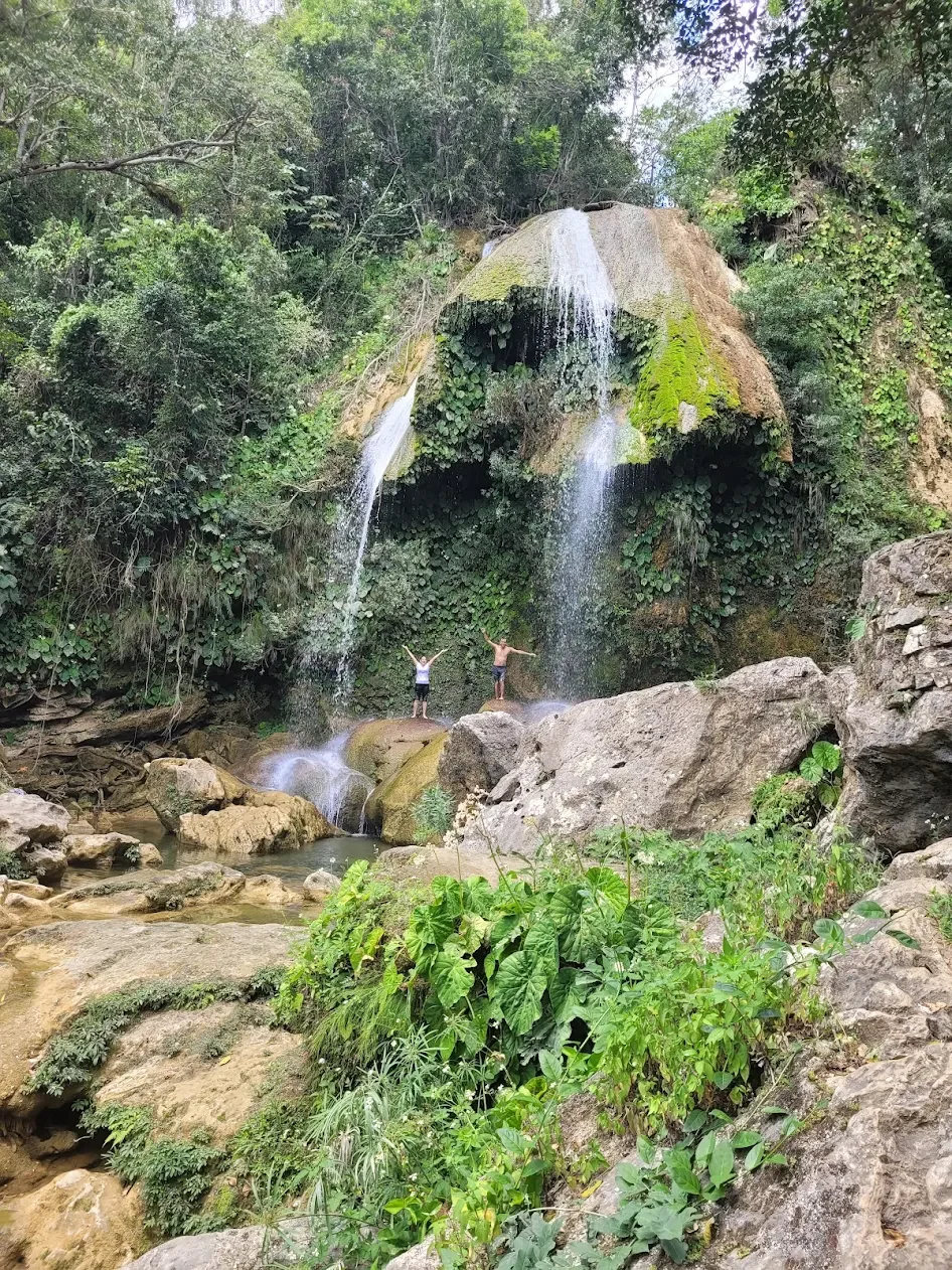 Deux clients heureux, debout sous une cascade au milieu d'une forêt luxuriante à Cuba.