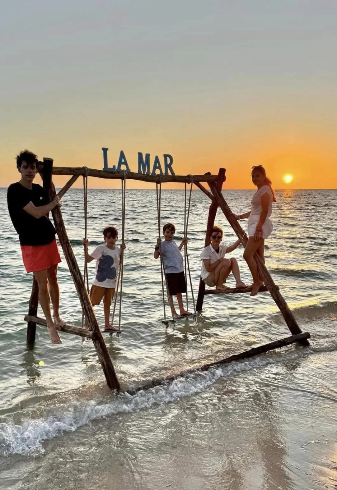 Groupe d'enfants jouant à Playa Ancon sur une balançoire en bois devant la mer et un joli coucher du soleil.