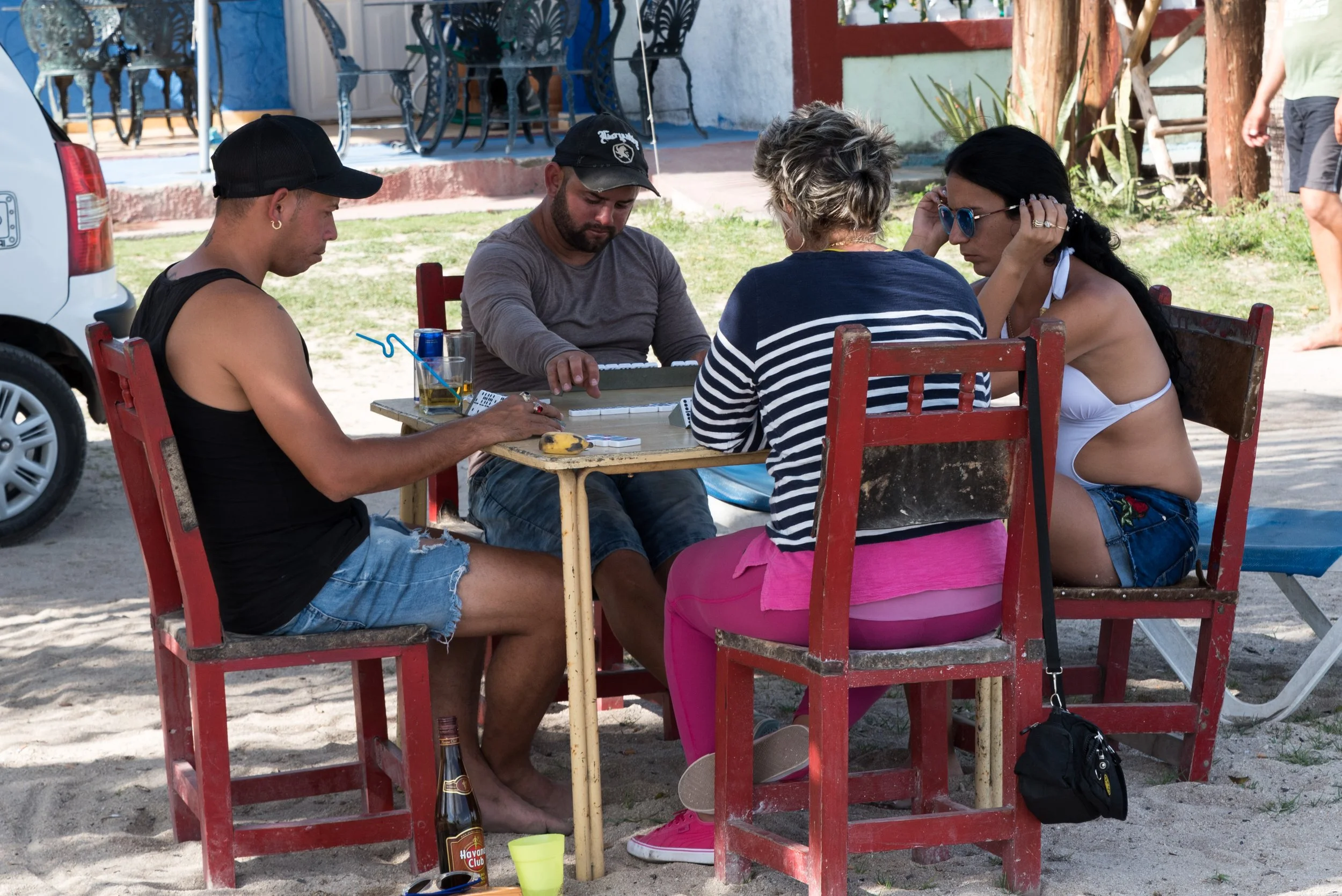 Groupe de quatre cubains jouant aux dominos dans la bonne humeur, avec des boissons devant eux.