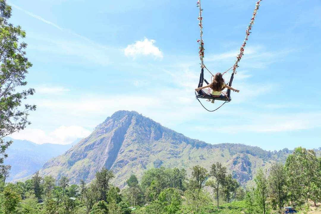Notre jeune voyageuse de 9ans profite du Sri Lanka, assise sur une balançoire décorée de fleurs, suspendue dans un paysage naturel avec des montagnes verdoyantes et un ciel bleu clair.