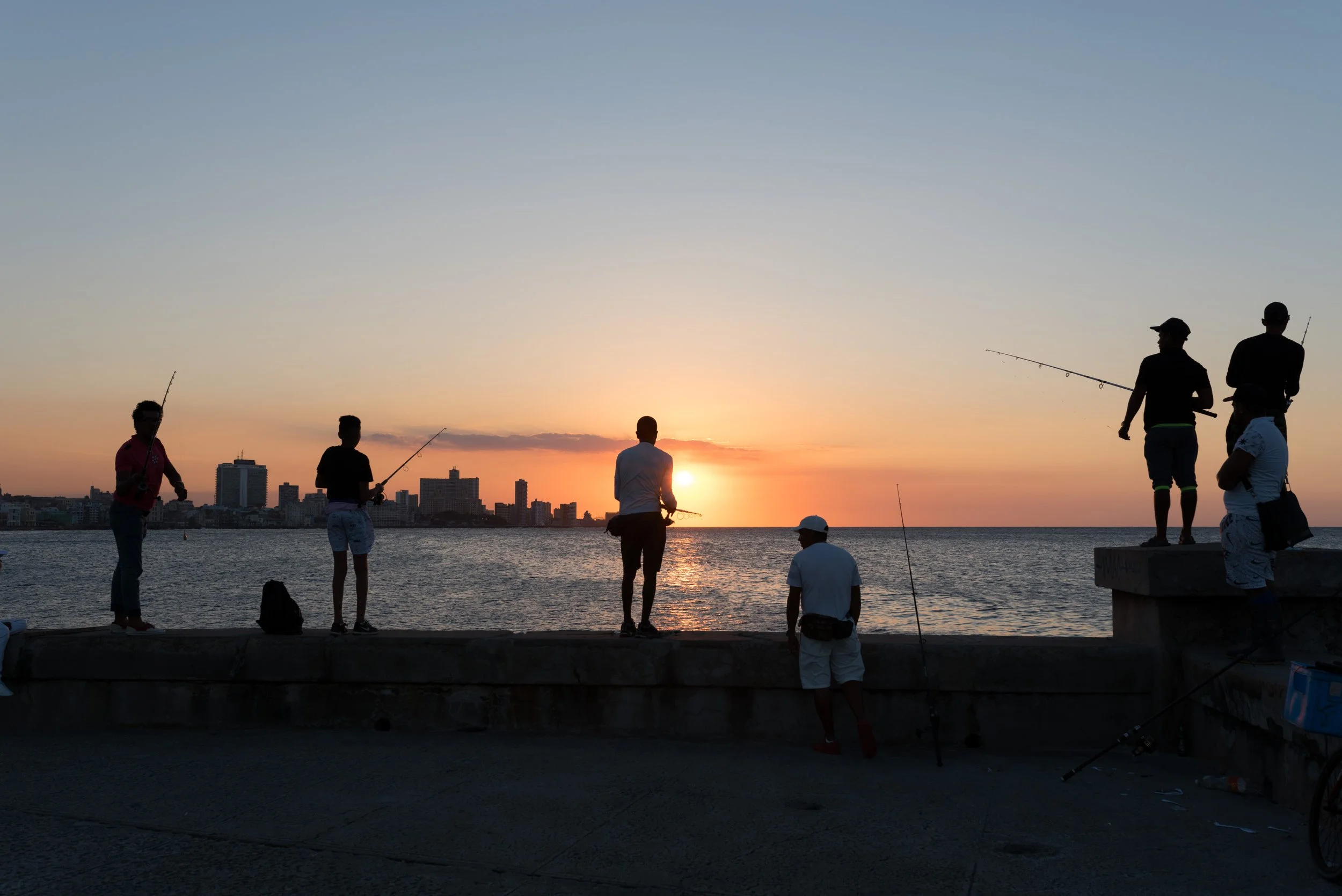 Groupe de personnes pêchant au moent du coucher du soleil sur une jetée de La Havane, avec une vue sur la ville en arrière-plan.