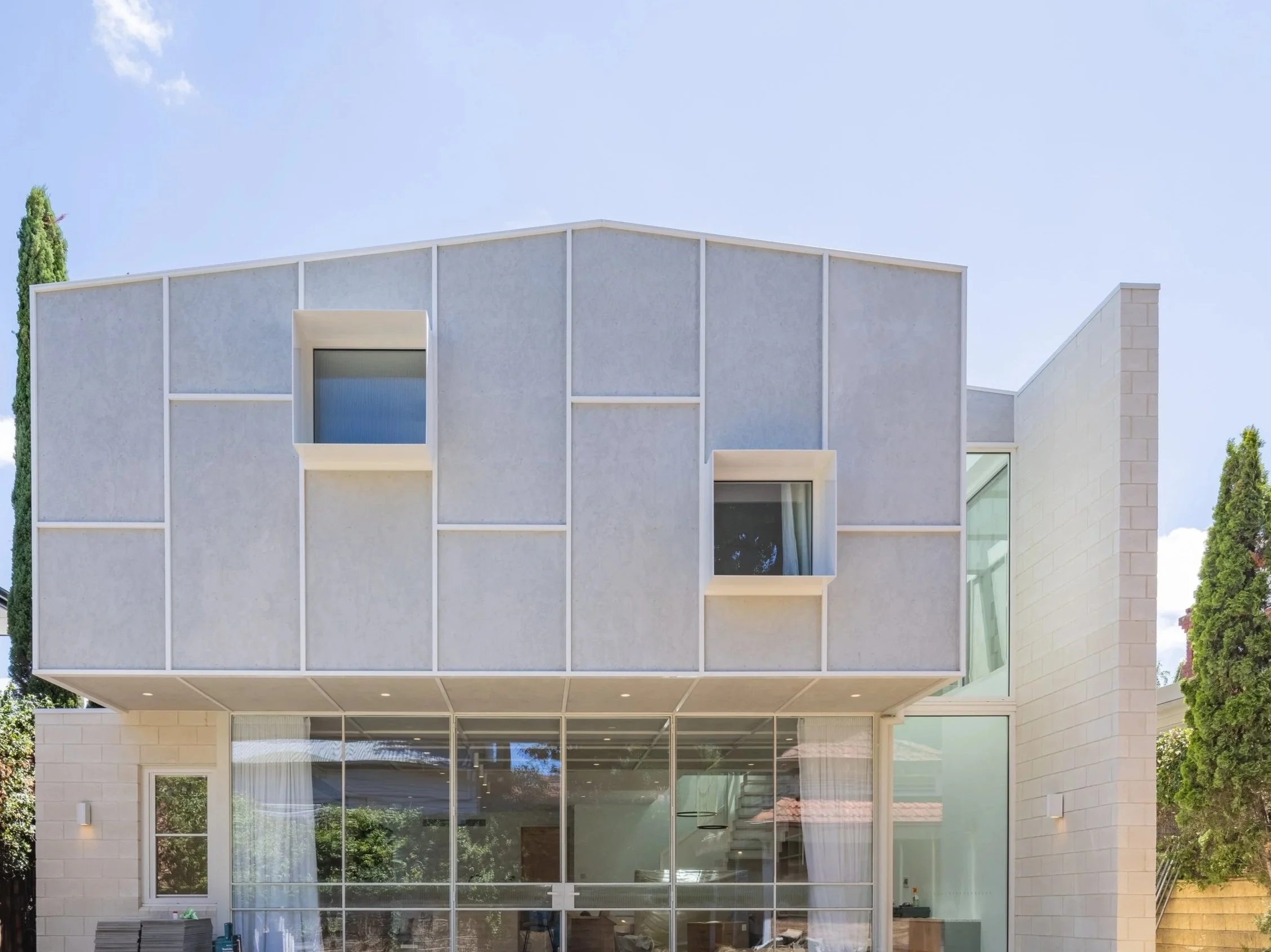 Modern bathroom with dark gray walls, a circular mirror, and two pendant lights with white globes. There are two oval sinks on a white countertop, a partial view of a toilet, and a textured lower wall panel.