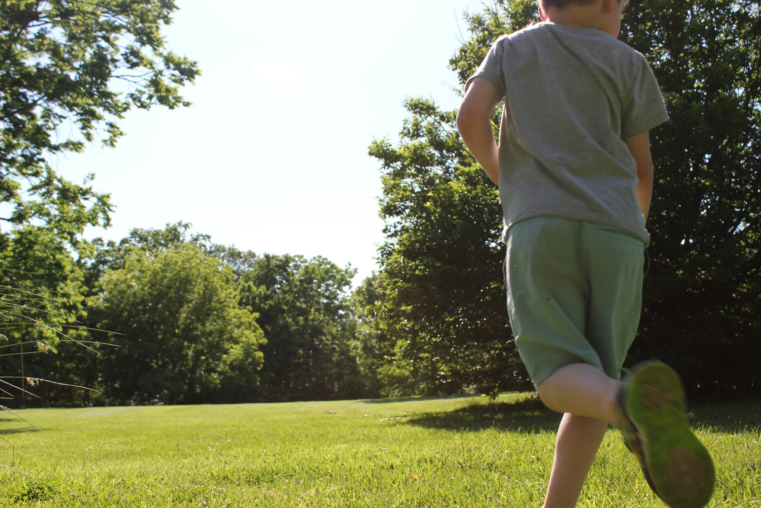 a boy running in the sunshine on the grass