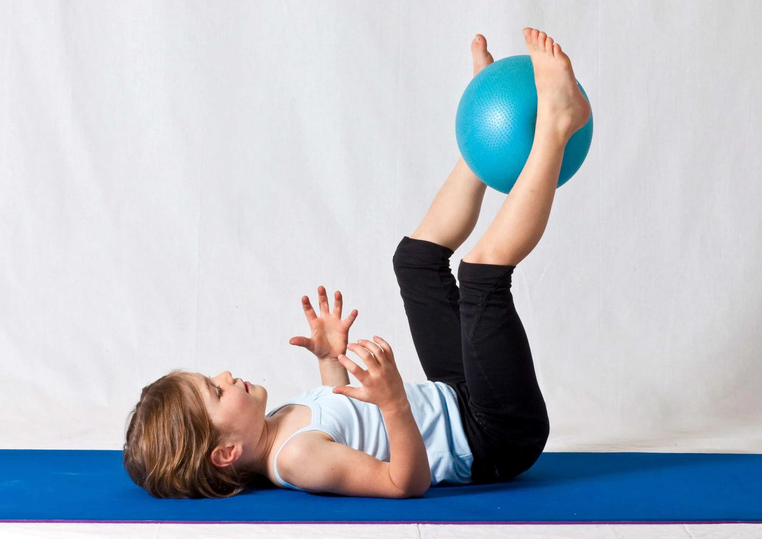 a child laying on the floor with legs raised and a ball between their feet