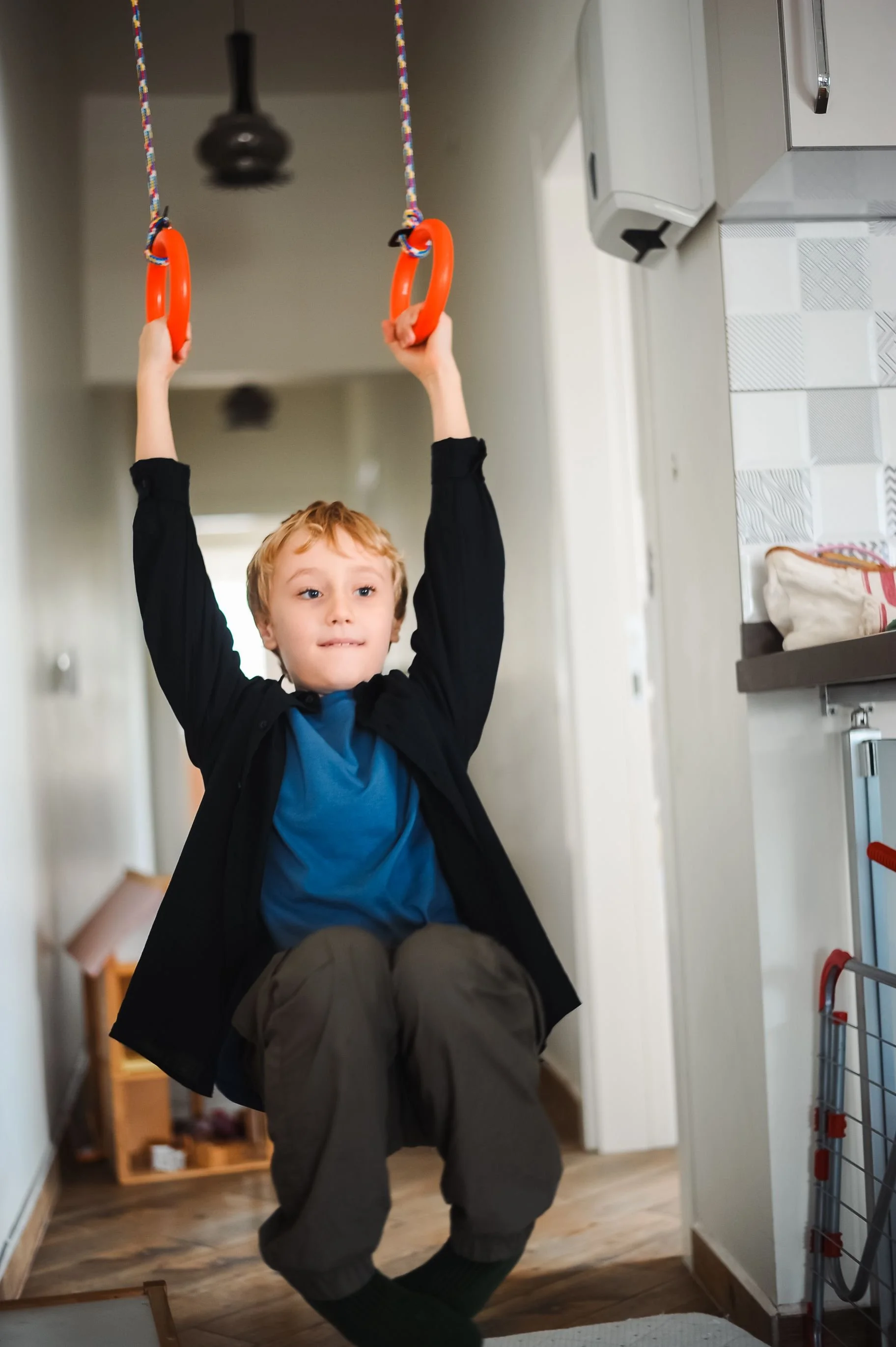 a boy swinging from orange handles with his legs off the ground