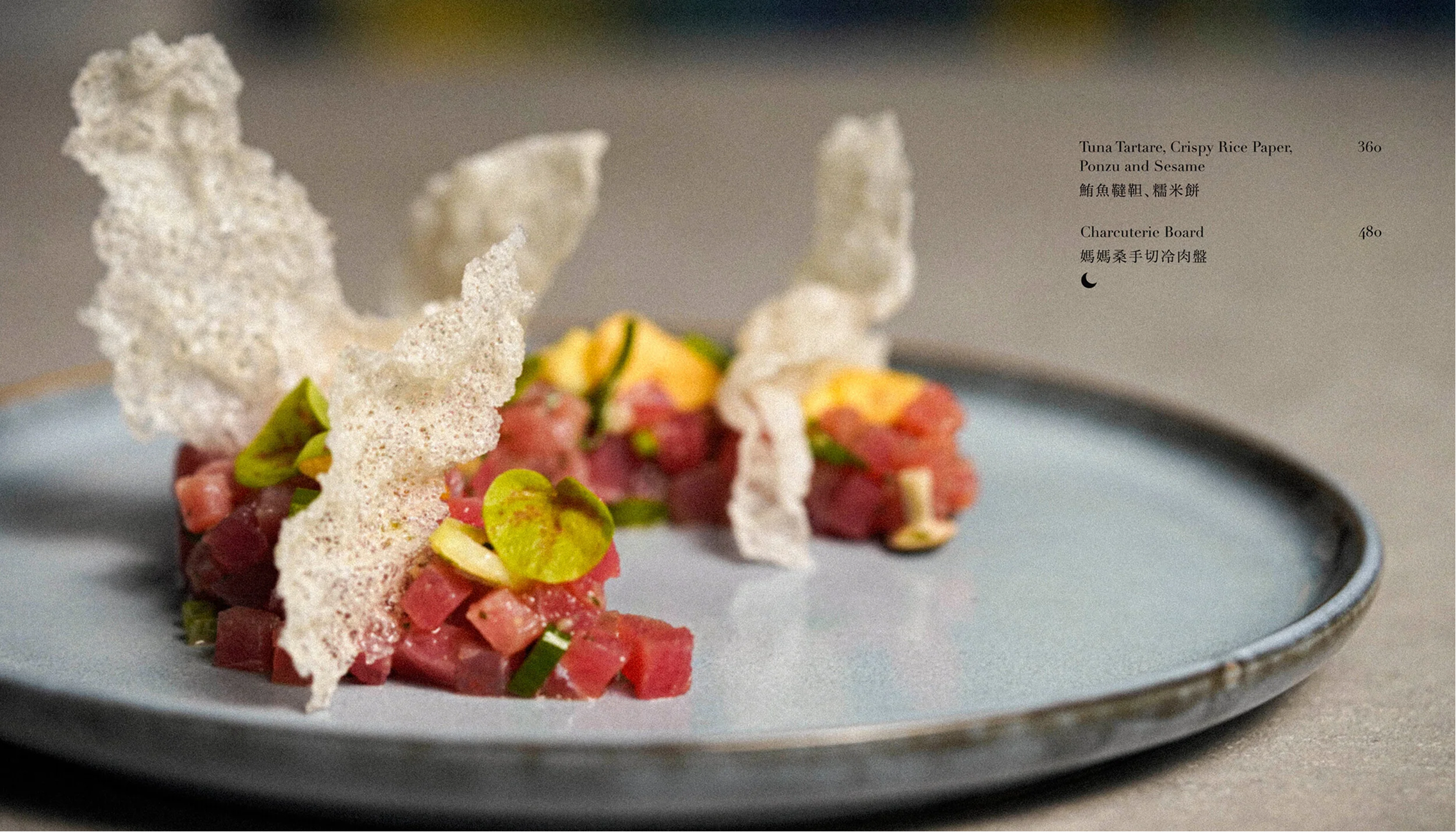 A plated dish featuring diced raw fish, green onions, and yellow garnishes with crispy rice paper and seaweed decorations, resembling a tuna tartare dish.