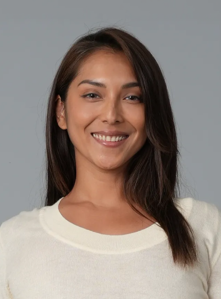 A woman with long dark hair smiling, wearing a white top, against a gray background.