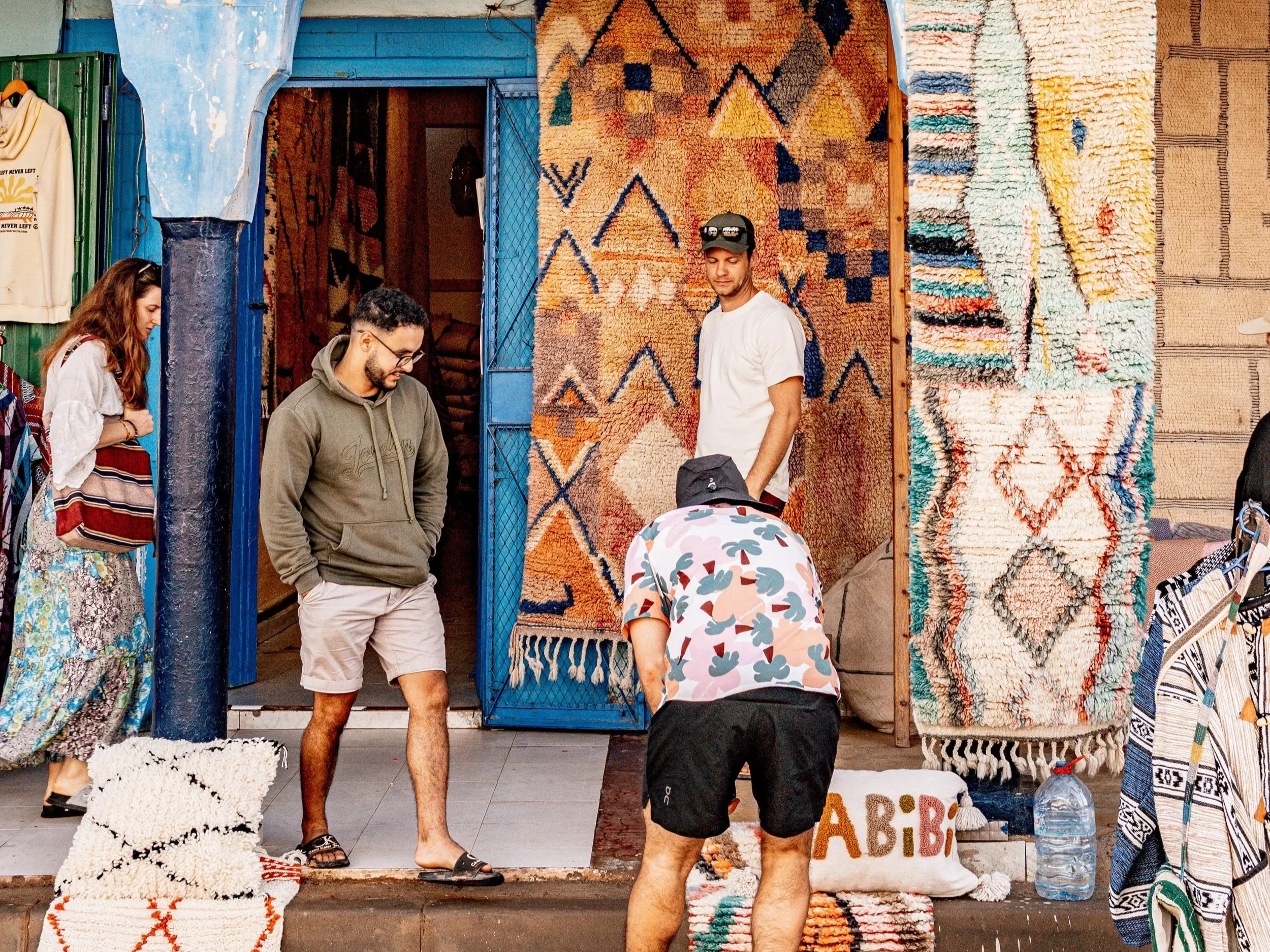 People browsing and shopping for colorful, patterned rugs at an outdoor market.