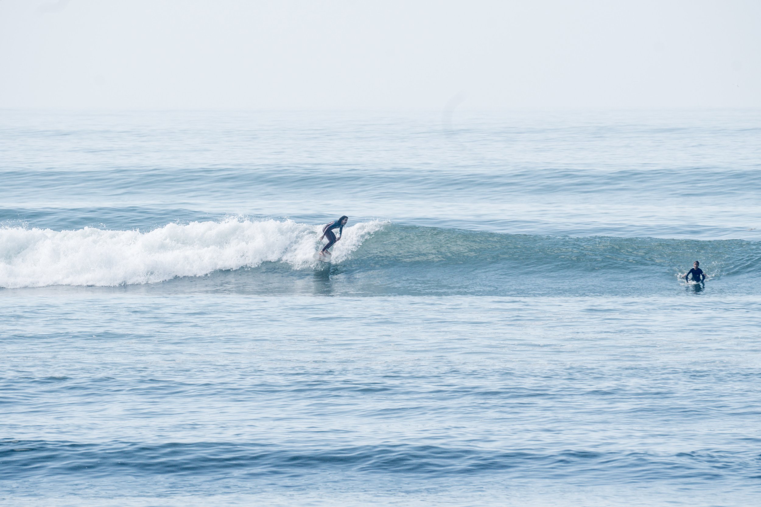 A person surfing on a wave in the ocean with another person standing in the water nearby.