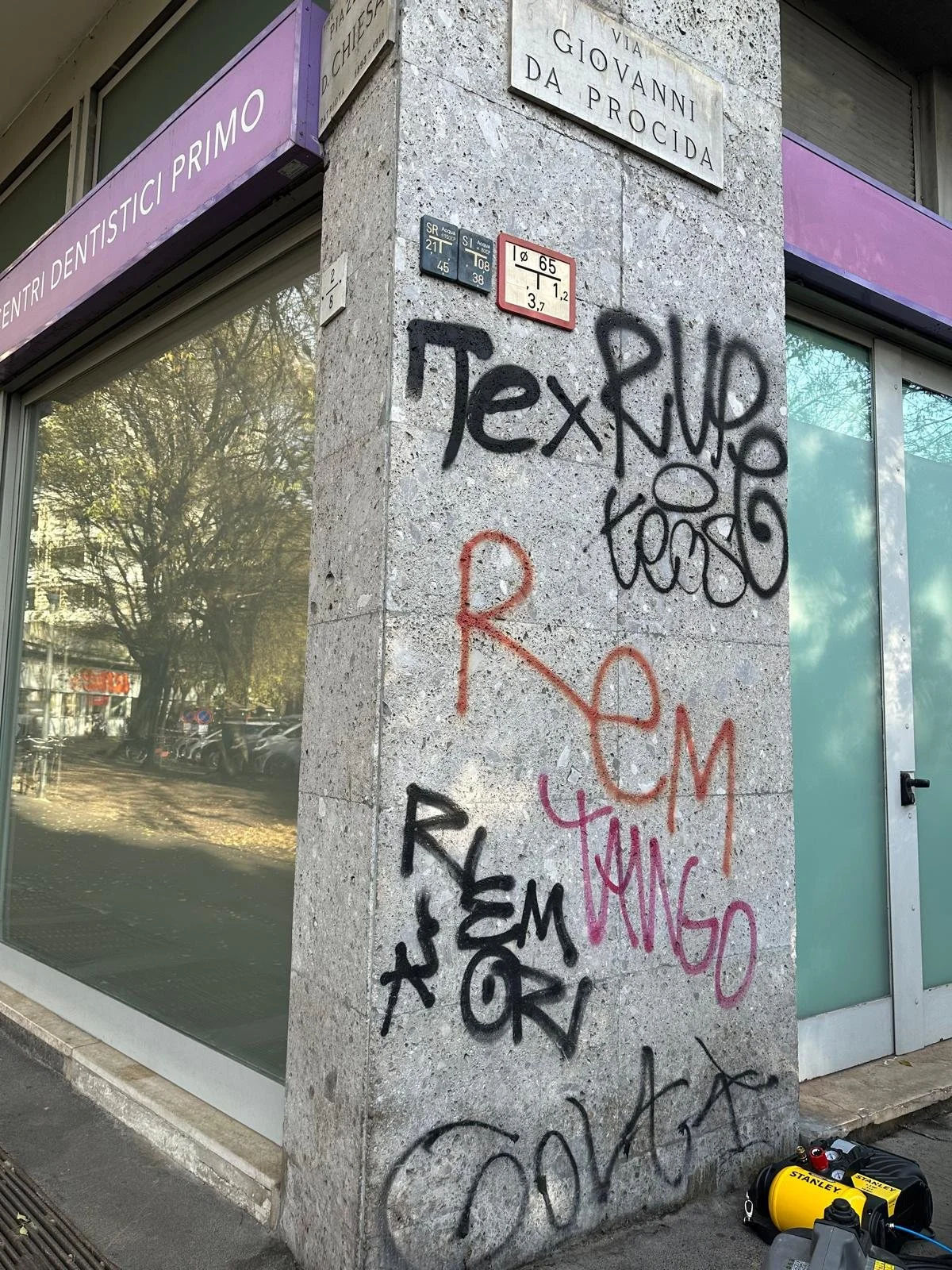 Mural di graffiti su un muro di pietra con diverse scritte in vernice, tra cui 'Tex' e 'Rome', accanto a un'entrata di un centro dentistico chiamato 'Centri Dentistici Primo'.