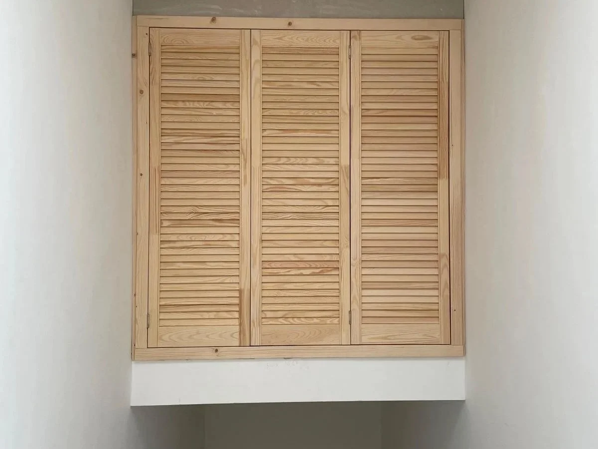 Wooden louvered closet door above a stairway as a storage solution.