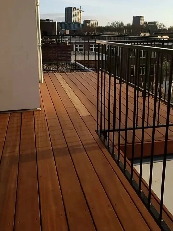 View from a balcony with wooden flooring and black metal railing, overlooking a city skyline with tall buildings and clear sky.