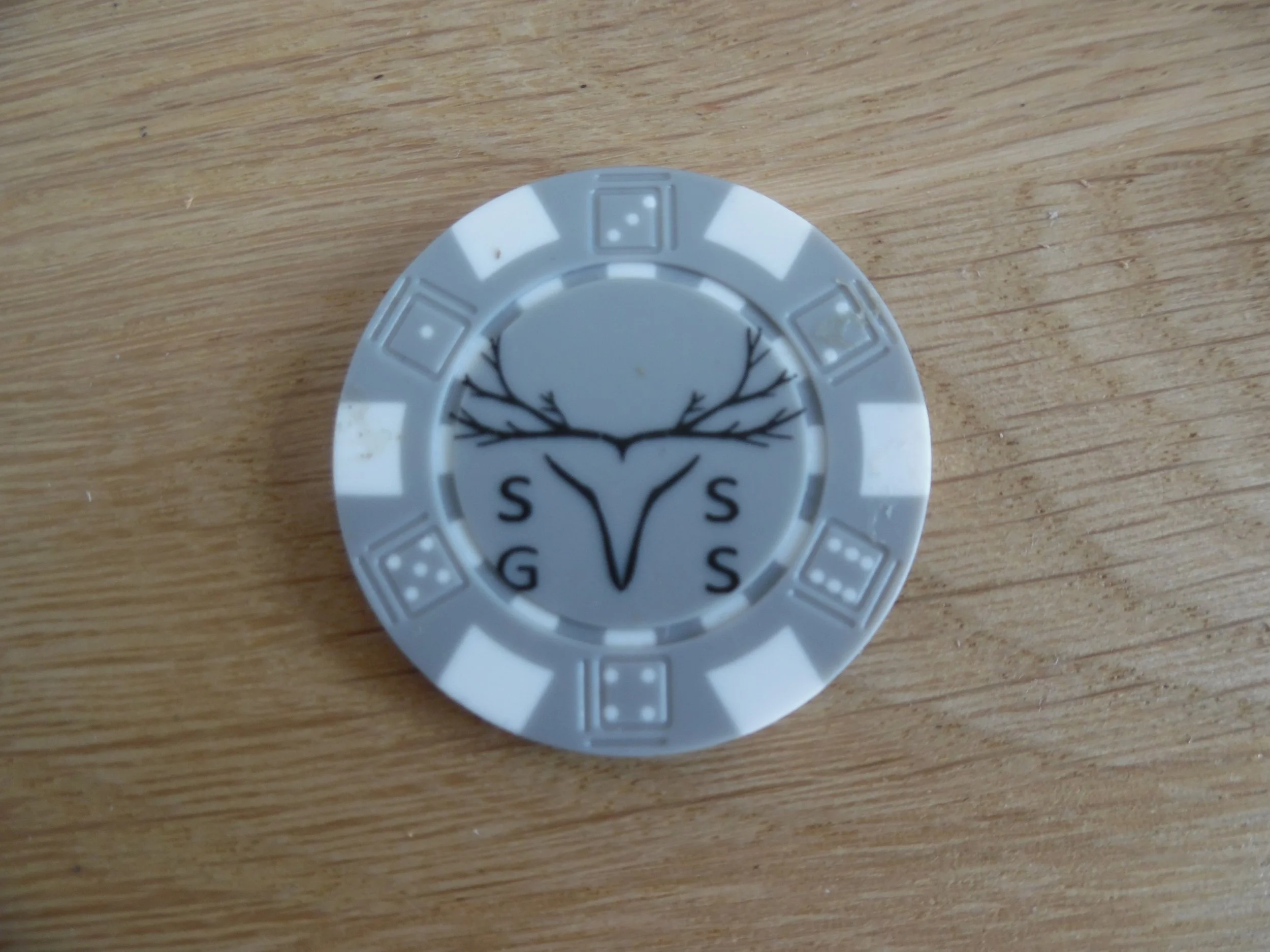 Casino chip with a tree and deer antlers design, and the letters S, G, and S around the logo, placed on a wooden surface.