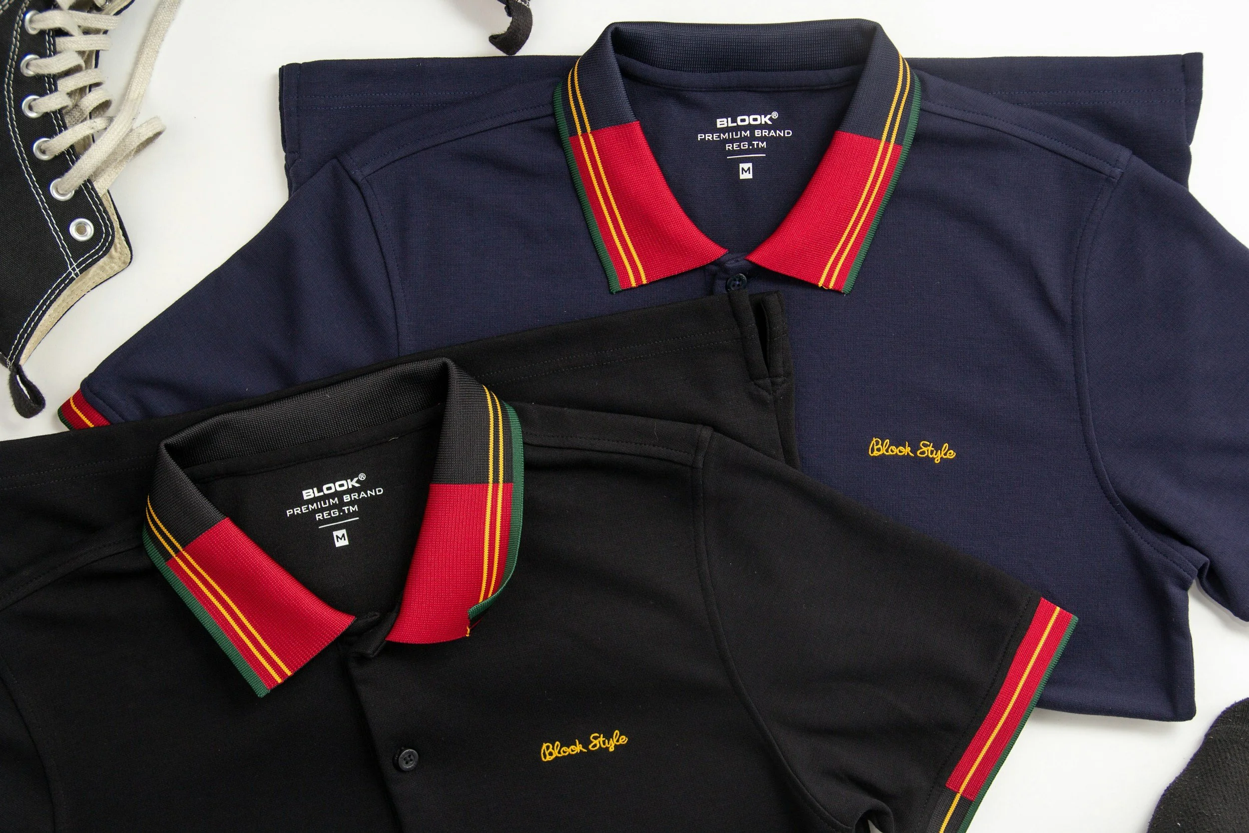 Two polo shirts, one black and one navy blue, with red, green, and yellow striped collars, laid flat on a white surface.