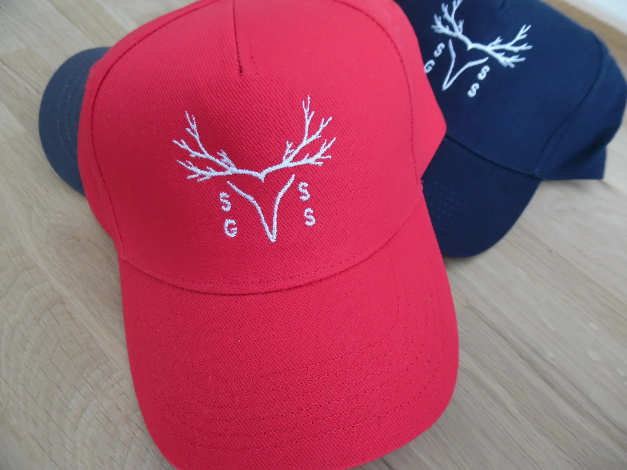 Red and navy blue baseball caps with a white pine tree logo and the letters S, G, S