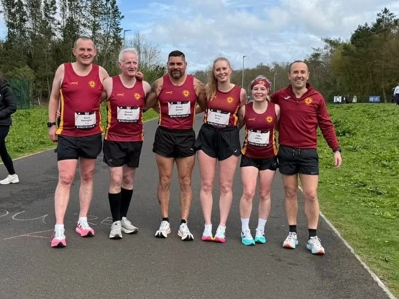 Six runners in matching maroon and gold athletic uniforms posing together outdoors on a track, smiling.