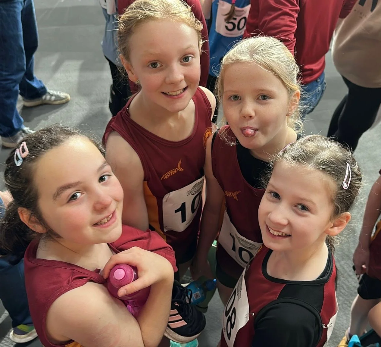 Four young girls in athletic wear at a sports event, smiling and posing for a photo.