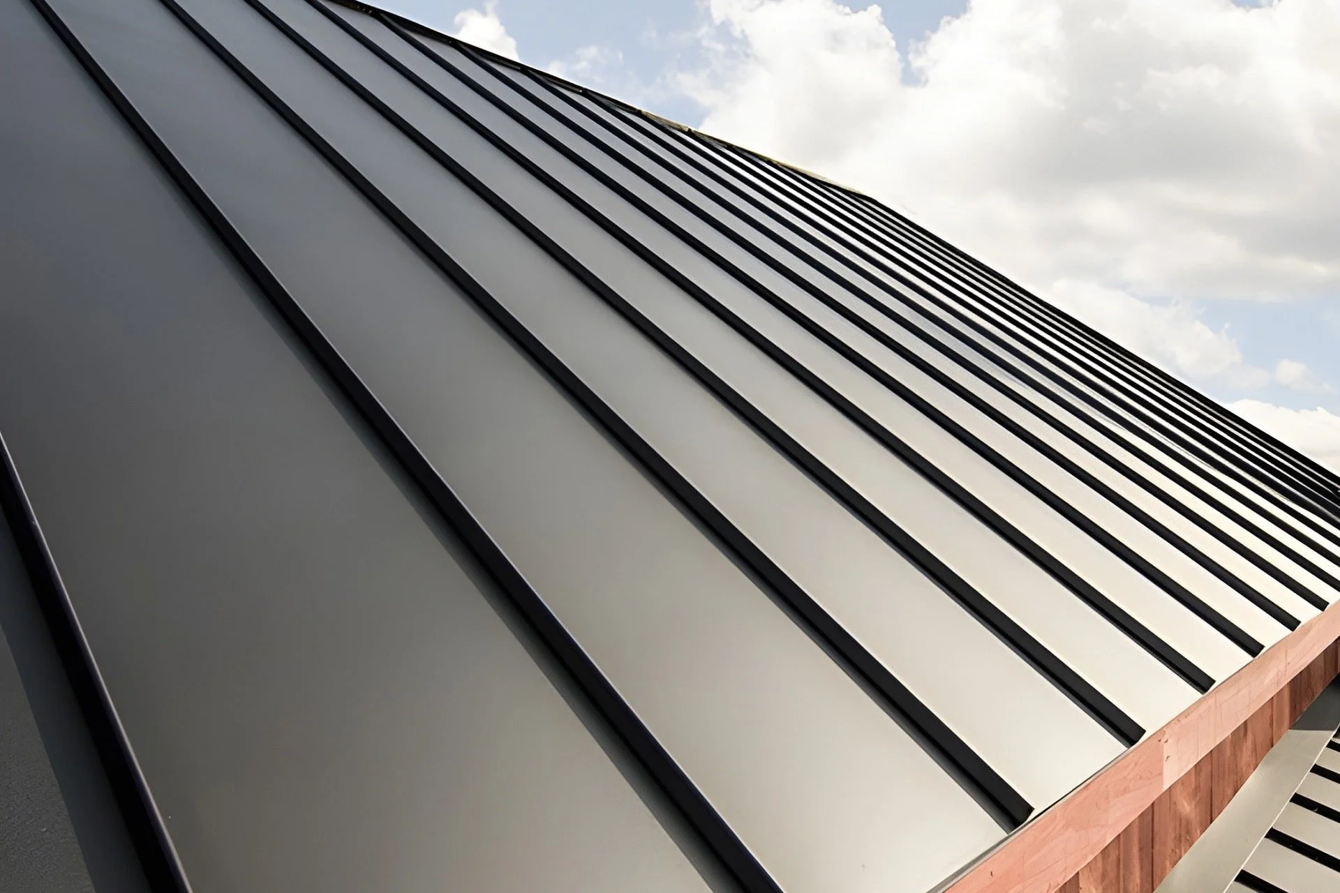 Close-up of a modern metallic building facade with vertical lines, viewed from below against a cloudy sky.