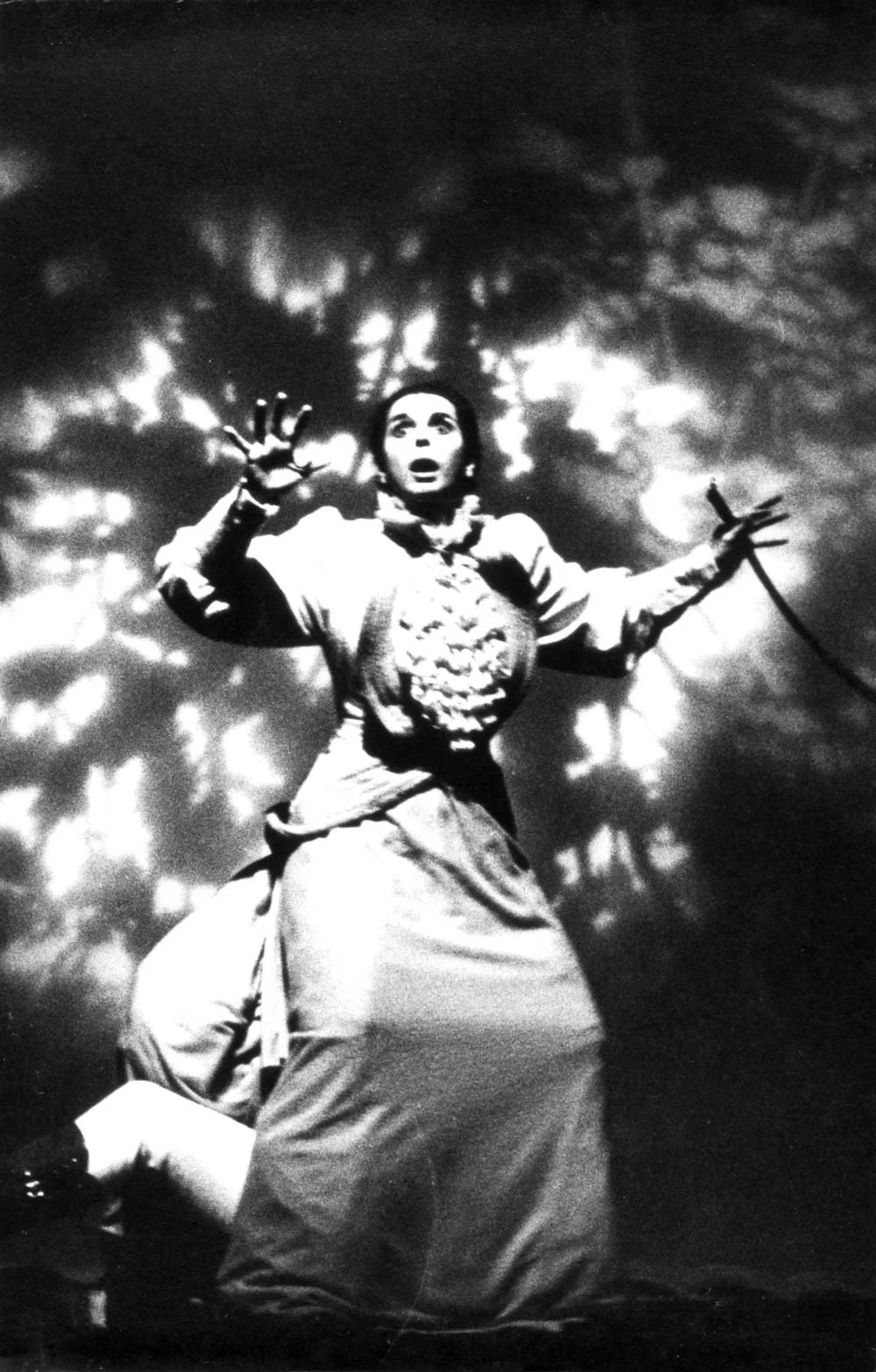 Imagem em preto e branco de uma mulher com expressão de surpresa, com uma mão levantada e outra segurando uma espada, em meio a uma iluminação dramática de fundo.