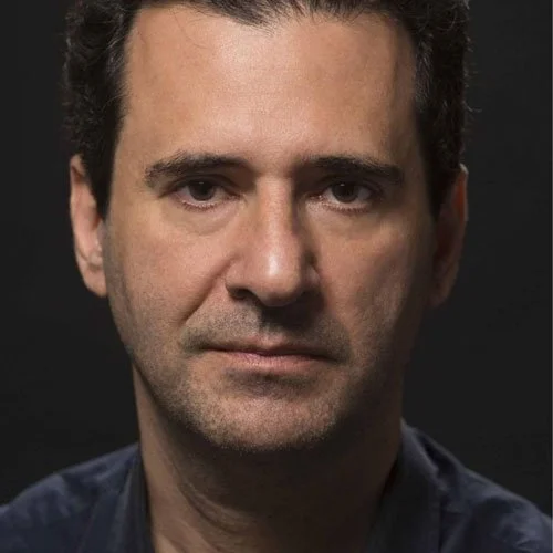 Retrato de um homem com expressão séria, cabelos castanhos escuros, pele clara e fundo preto.