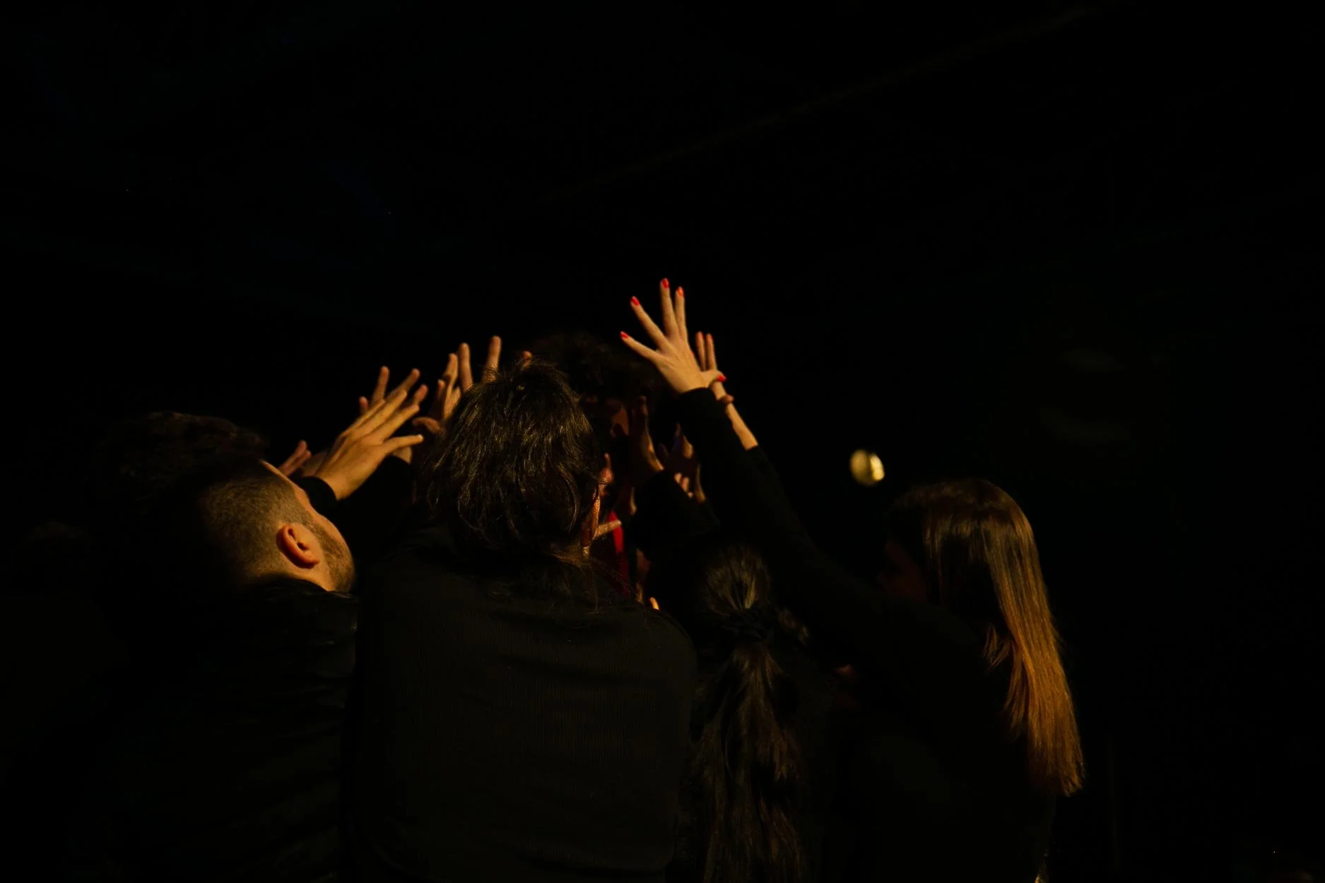 Grupo de pessoas com as mãos levantadas em um ambiente escuro