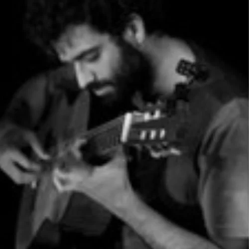 Homem tocando violão, com barba e cabelo cacheado, em uma foto em preto e branco.