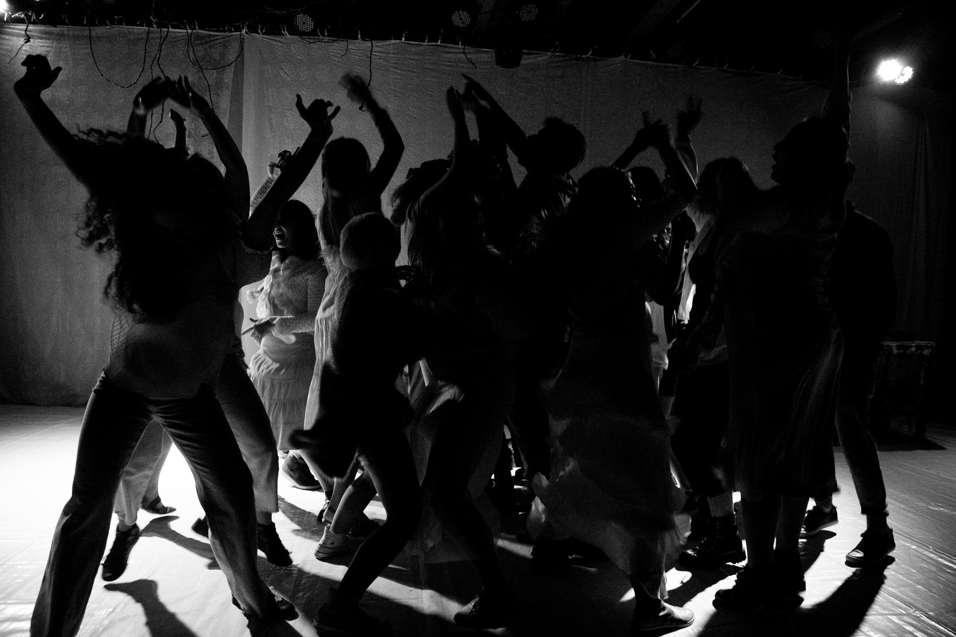 Silhuetas de pessoas dançando em uma festa ou evento, com iluminação fraca e fundo escuro.