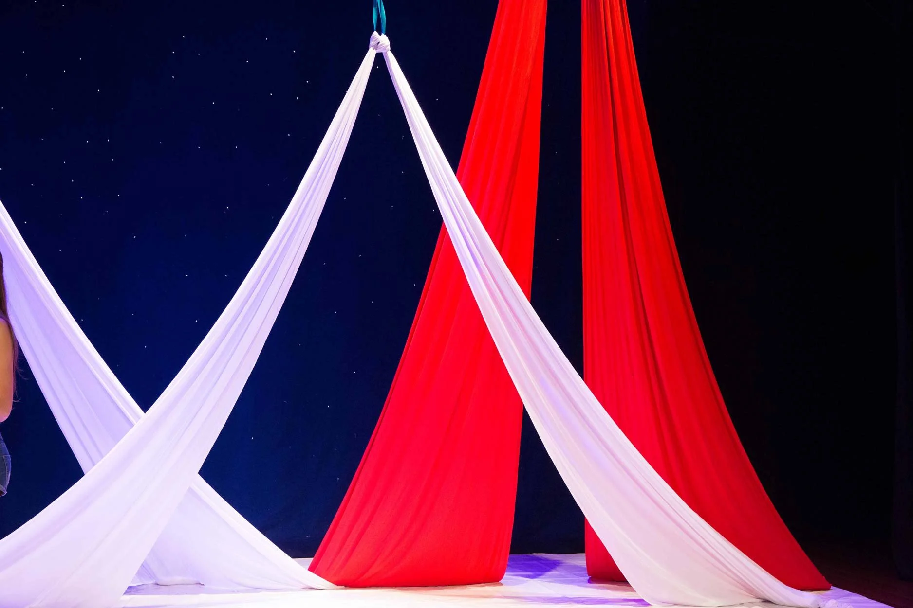 Tecidos brancos e vermelhos suspensos, formando um cenário artístico com céu estrelado de fundo.