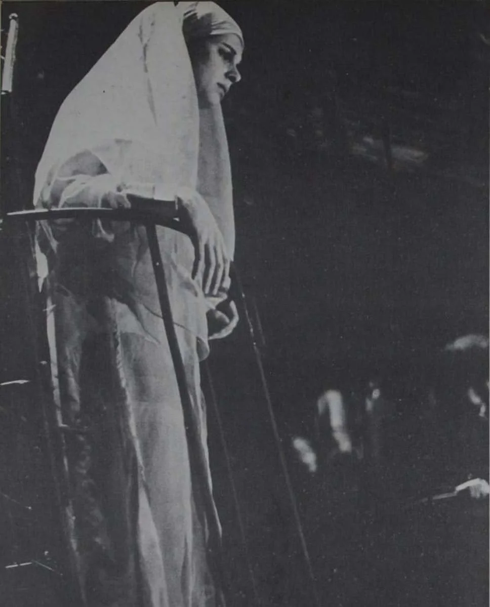 Mulher idosa com véu na cabeça, segurando um bastão, em uma caminhada solitária.