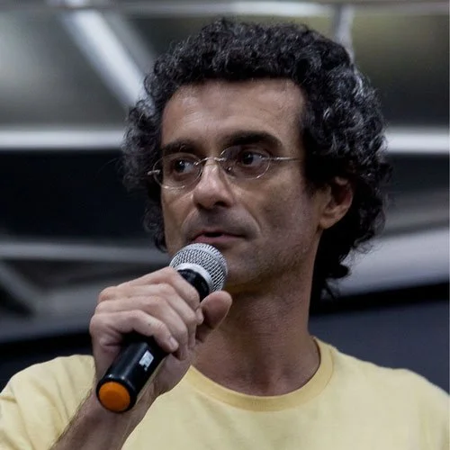 Homem com óculos de armações finas falando ao microfone.