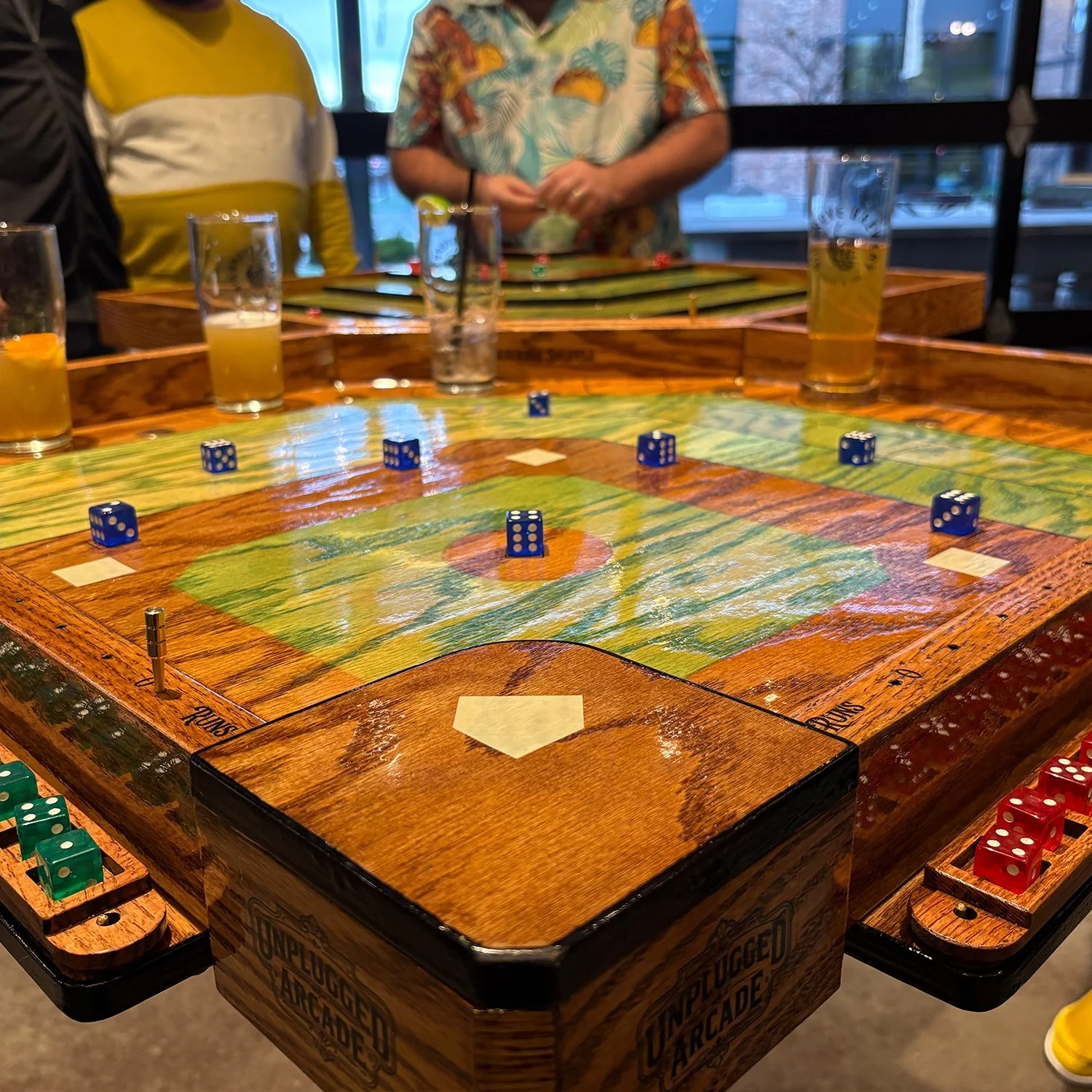 A large wooden game board with water on top, surrounded by a wooden border. Several red dice are placed on the board, with one blue die in the corner. The background shows green grass.