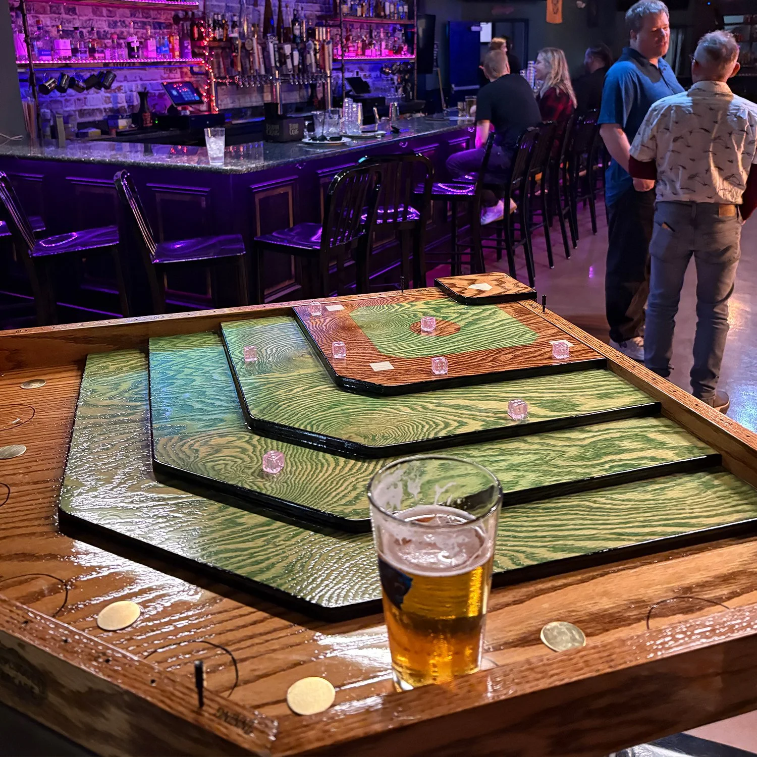 A tabletop baseball themed shuffleboard game set on a black stand outside on green grass with a wooded background.