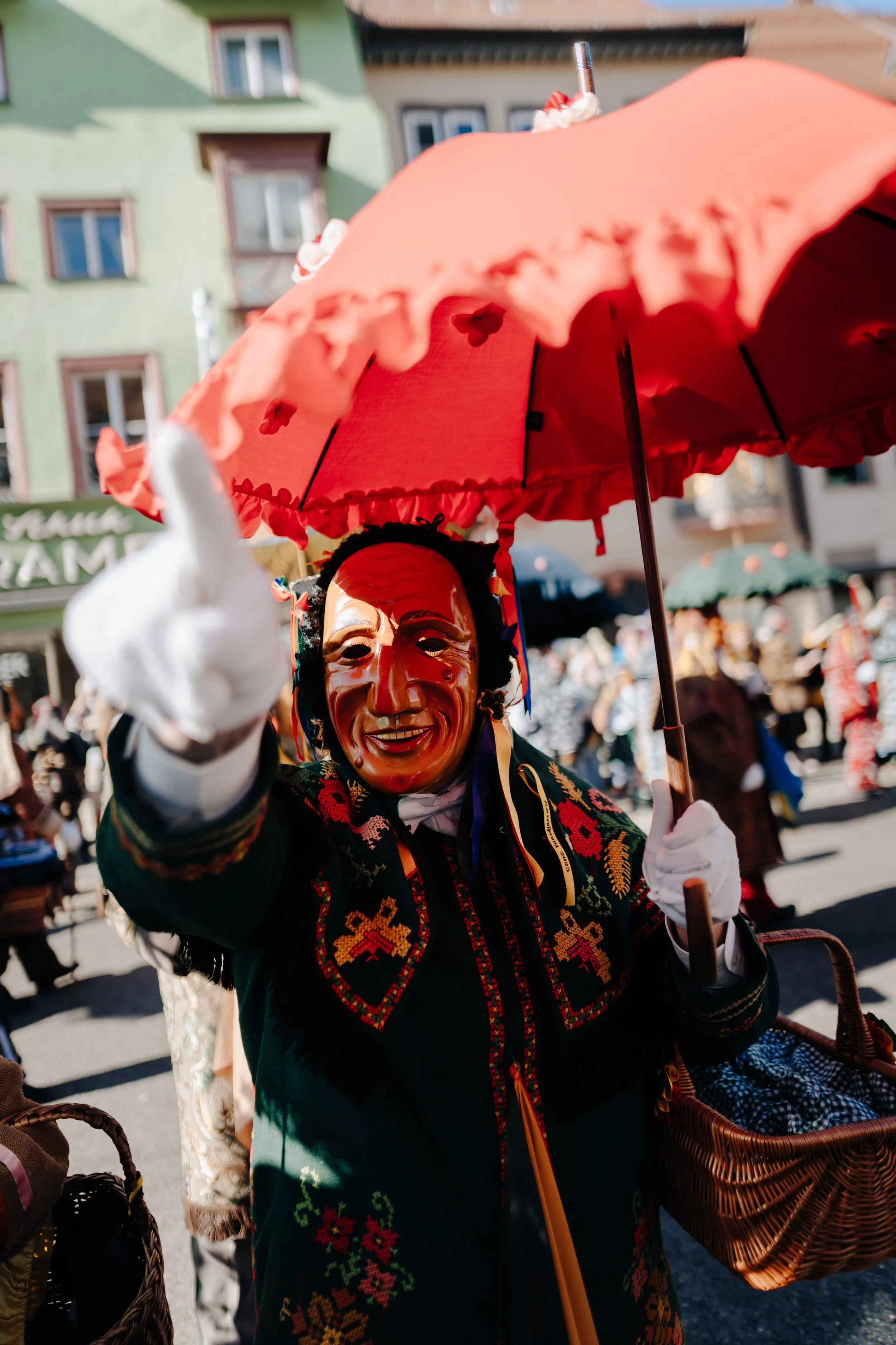 Person in traditionellem Kostüm und Maske, die einen roten Regenschirm hält, während eines Festivals im Freien.